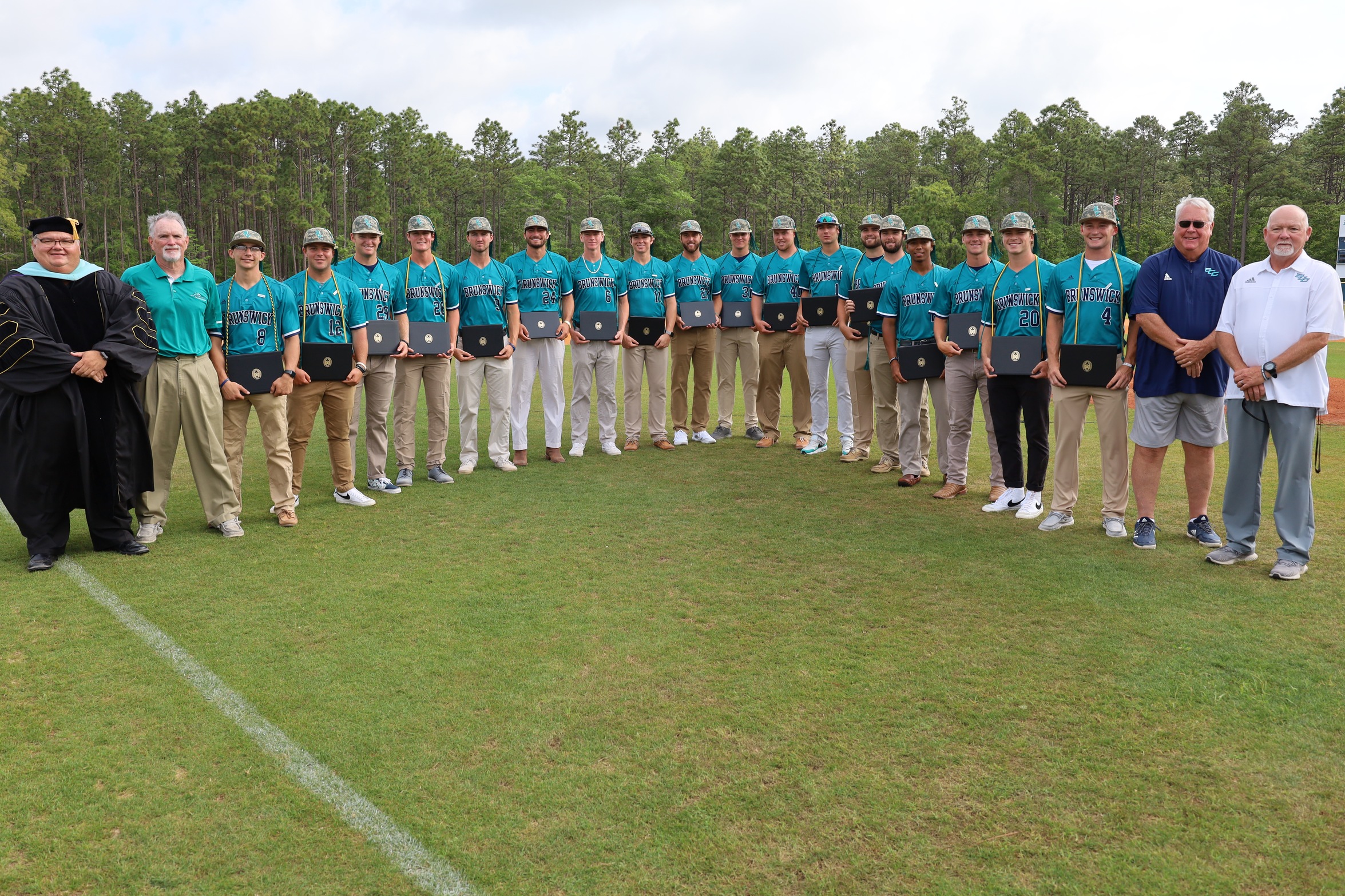 Baseball players join President Smith and coaches in a group photo on Founders Field on Graduation Day.
